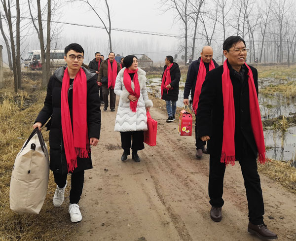 商会慰问团成员在熊桂祥会长的带领下，手拎慰问物品，正踏着乡间泥土路走向慰问特困户家中